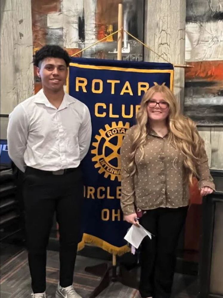 Caleb Lowe and Keiarra Maynard standing in front of a Rotary Club flag