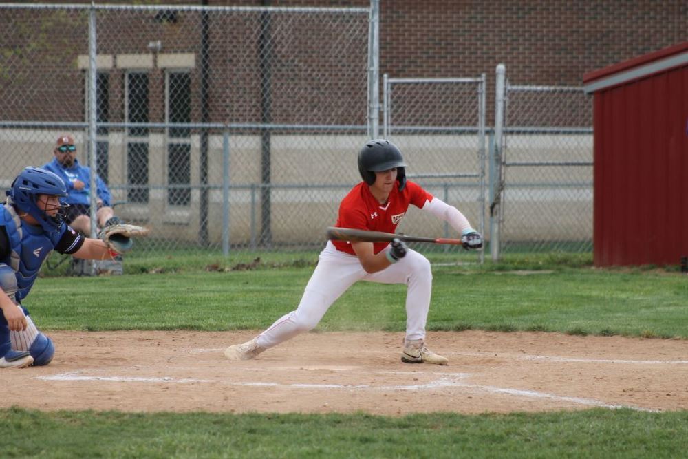 Male baseball player in red uniform top and white uniform pants holding a baseball bat out in front of him to bunt a ball 