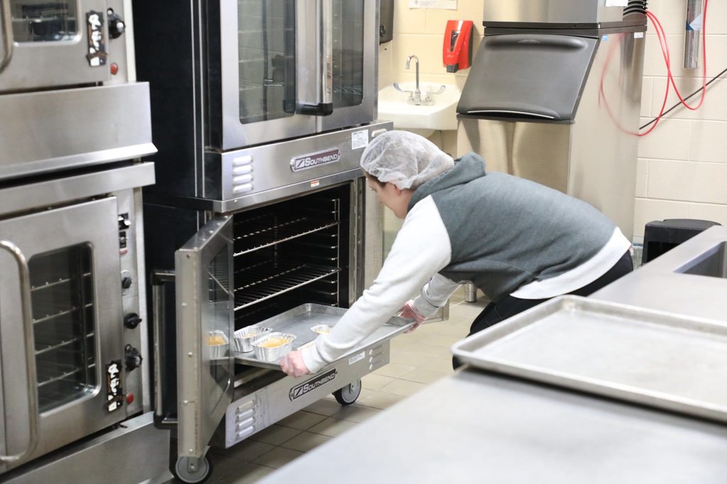 Cafeteria cook putting baking sheet full of pumpkin bread tins into oven