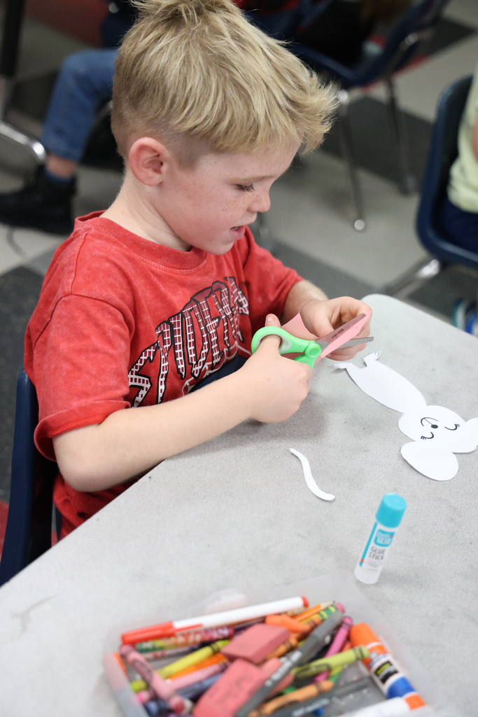 Student cutting pink piece of paper with green scissors