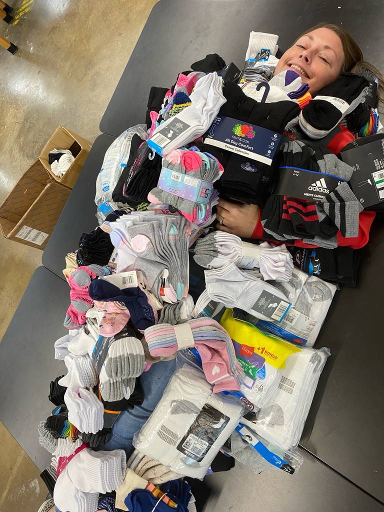 A female teacher laying on a black desk with several pairs of socks covering her body