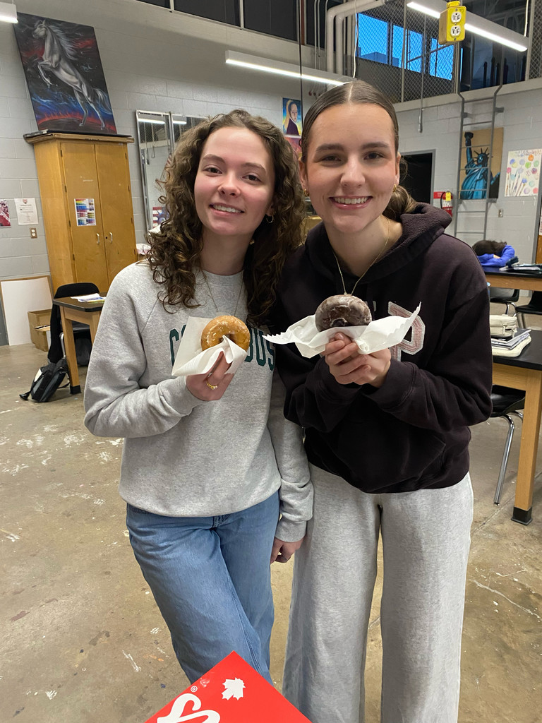 Two smiling female students holding donuts in napkins