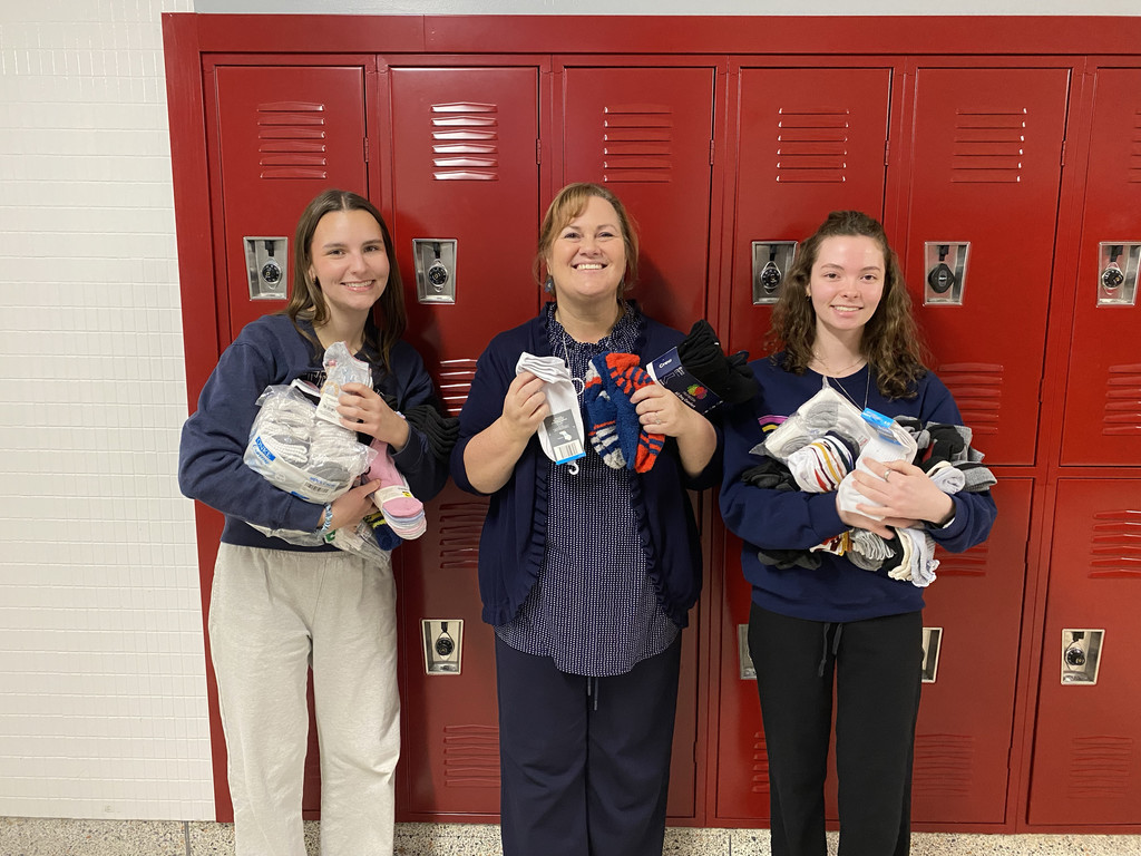 A female teacher standing with two female students smiling and holding several pairs of socks