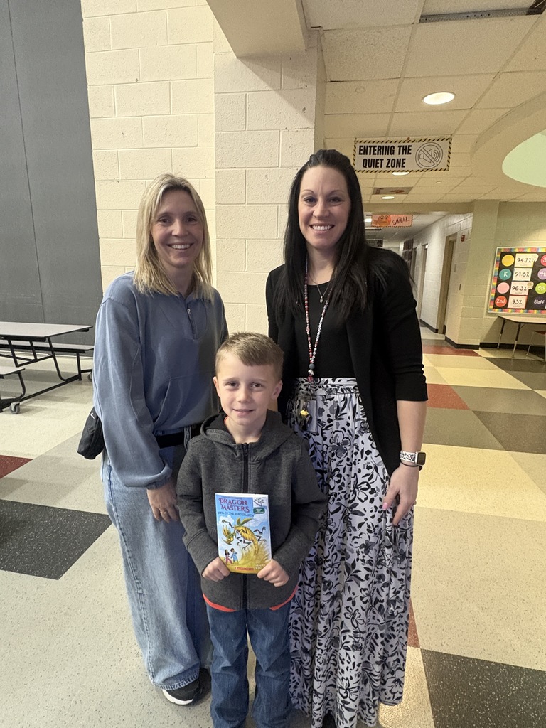Student posing with his new book, smiling in front of his mom and teacher