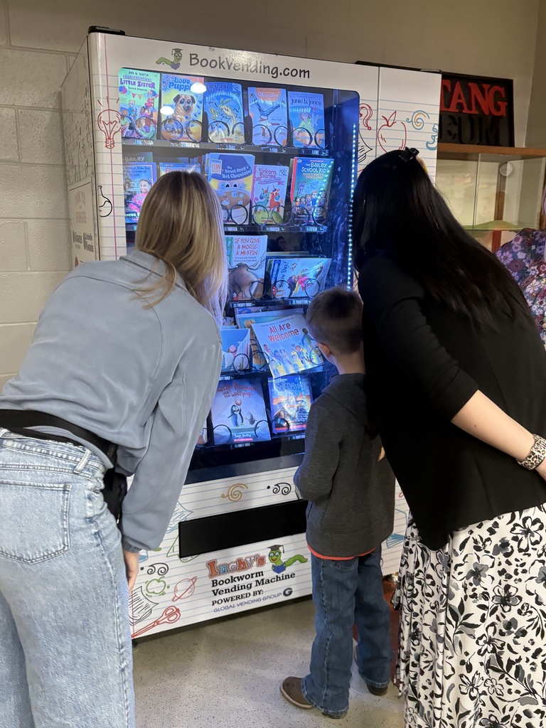 Student selecting a book from the book vending machine while his teacher and mom watch