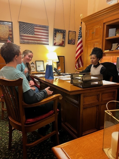 Whs Student smiling at camera as she and CHS student speak with government representative in an office