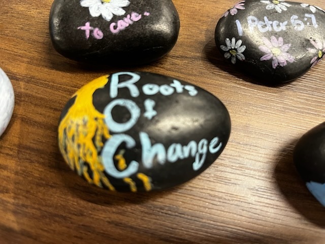 Painted Rock, colored black with roots of change written in white and a tree with dangling roots in yellow