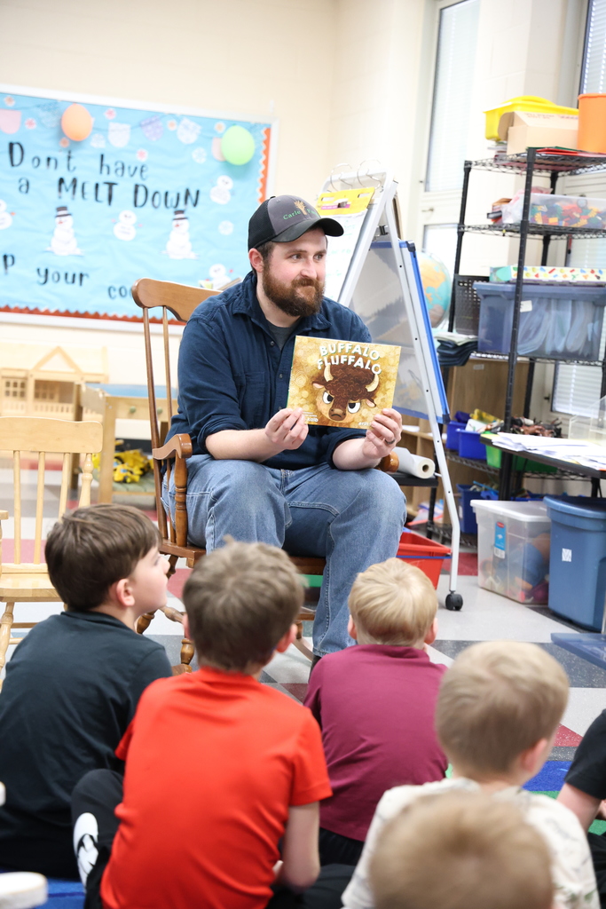 Man in hat reading a book to students 