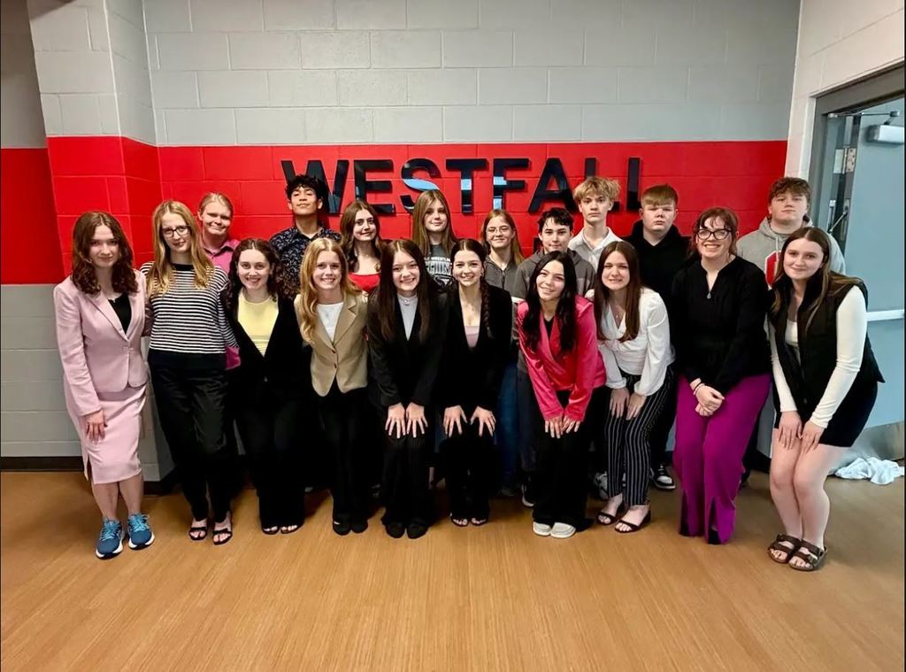 Female and male students dressed professionally, posing and smiling in front of a wall that reads Westfall