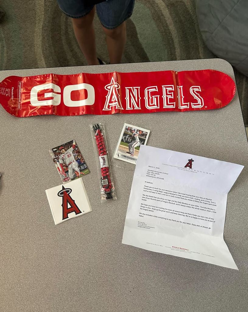 Deflated long balloon that reads Go Angels, two baseball cards, a sticker with the Angels logo and a letter from the Angels sitting on a desk