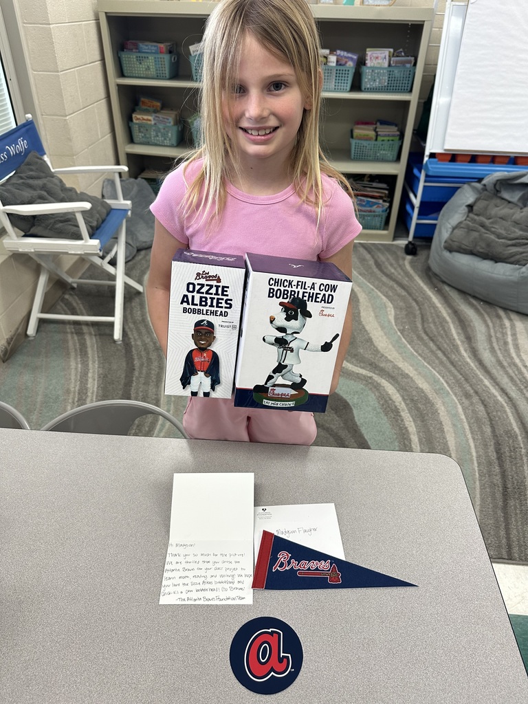 Madyson holding two boxes containing bobbleheads with a letter, sticker and pennant on the table