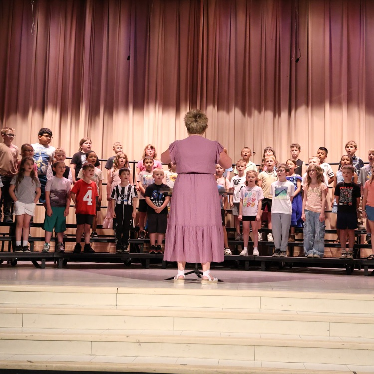 students standing on stage risers with music teacher standing in the center facing students 