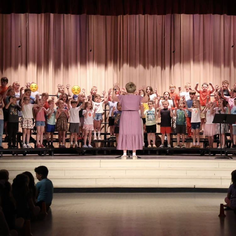students standing on stage risers with music teacher standing in center facing students 