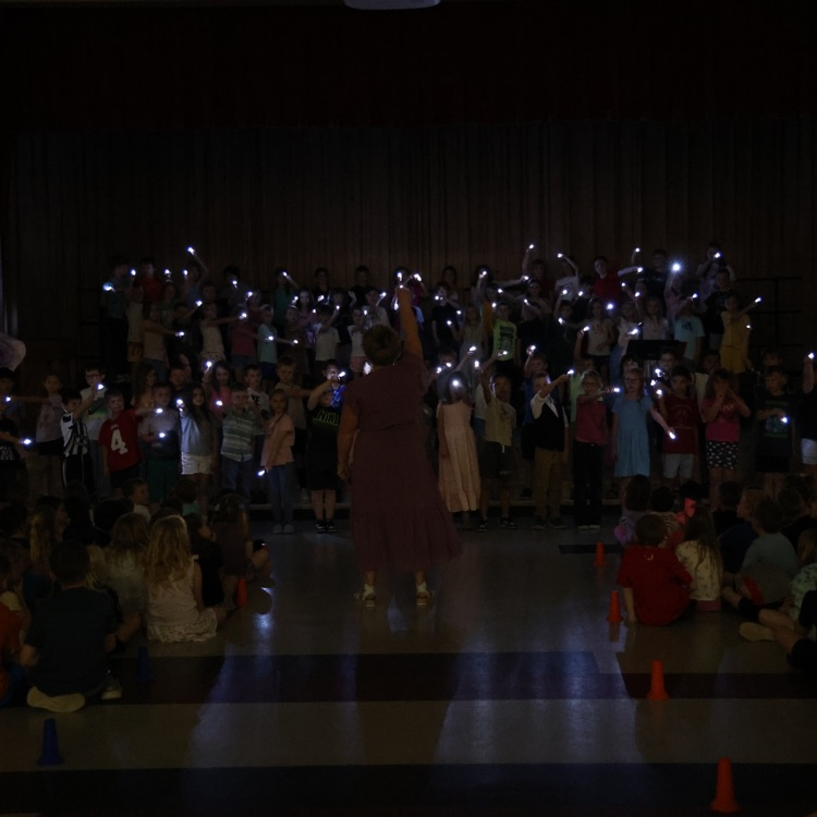 students on a dark stage holding lit flashlights