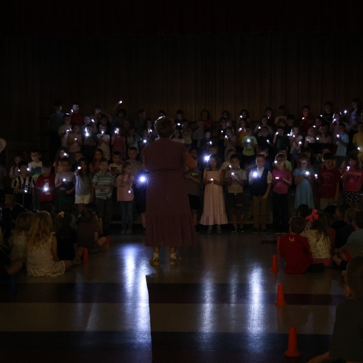 students on a dark stage holding lit flashlights