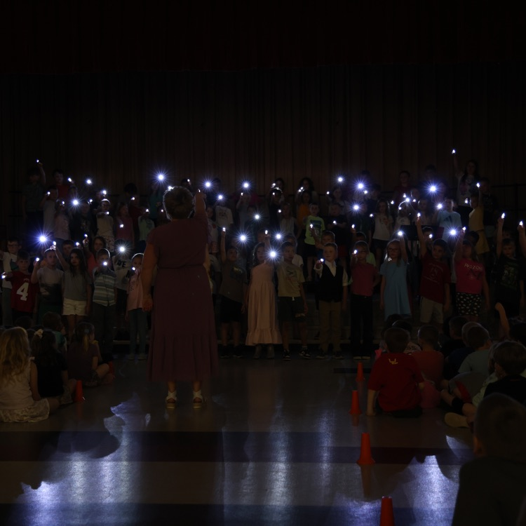 students on a dark stage holding lit flashlights