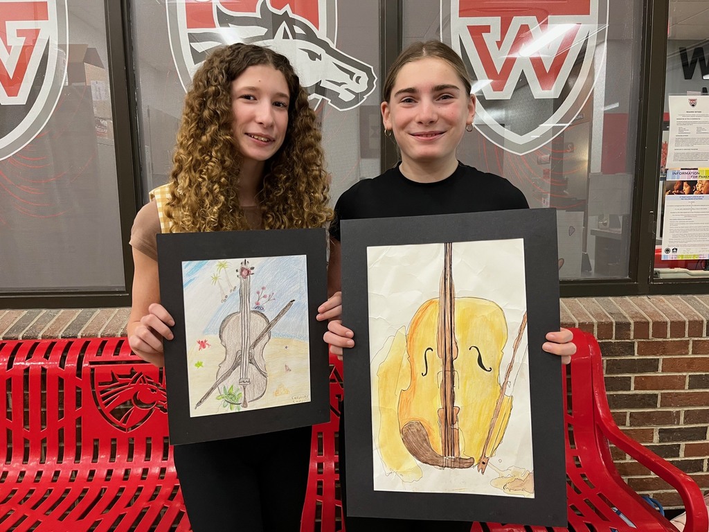Two female students holding artwork of colorful violins