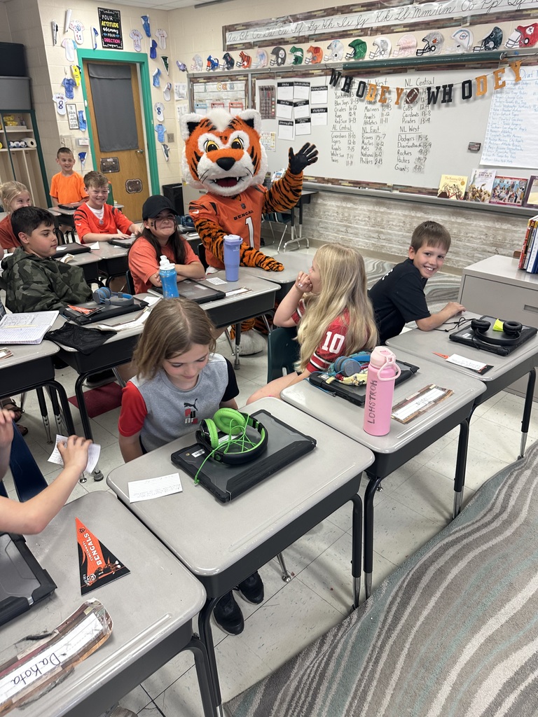 Cincinnati Bengals mascot posing in front of white board with team names listed with students sitting at their desks 