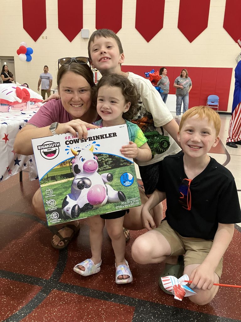 A family smiling at the camera while holding a box containing an inflatable cow sprinkler