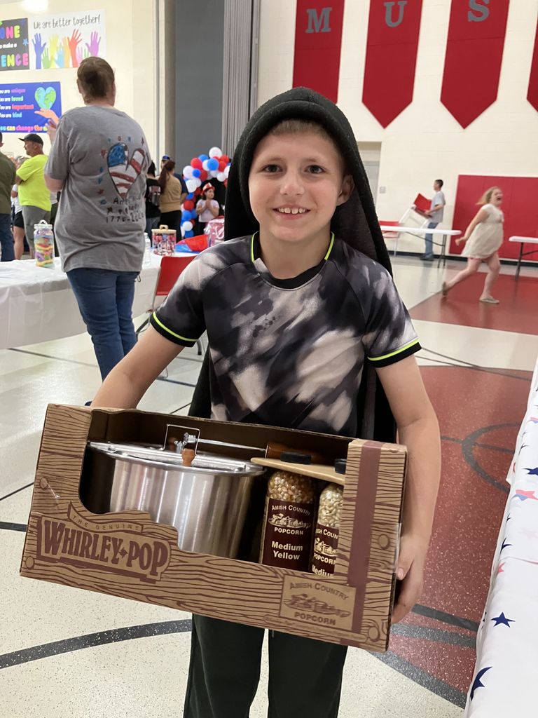 A student smiling holding a box of Whirley Pop machine and popcorn kernals