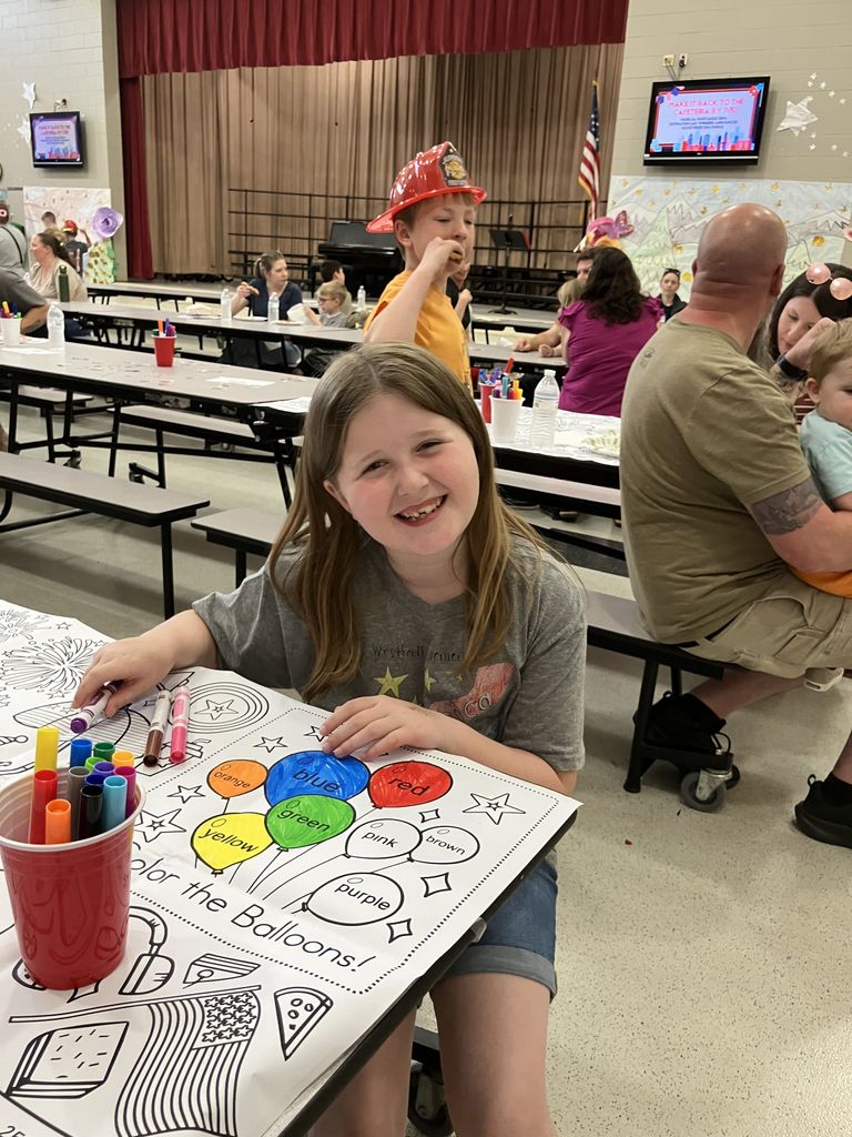 A student smiling at the camera while coloring a large coloring sheet