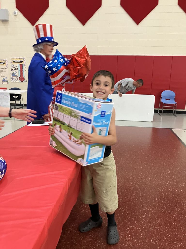 A student smiling while holding a family swimming pool in a box while Uncle Sam walks behind him