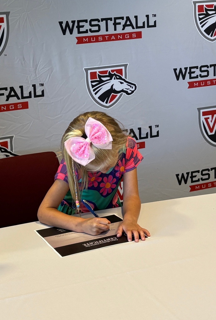 Kindergartener signing a certificate with the Westfall backdrop in the background