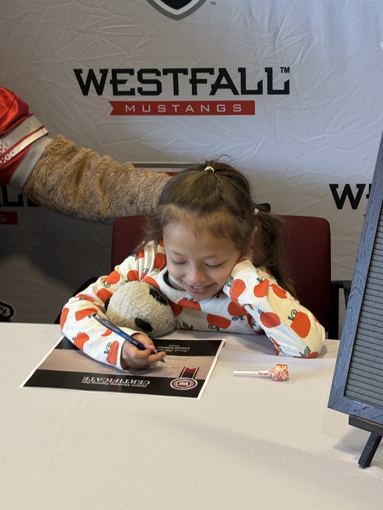 Kindergartener signing a certificate with the Westfall backdrop in the background and a sign that reads Welcome Future Mustang