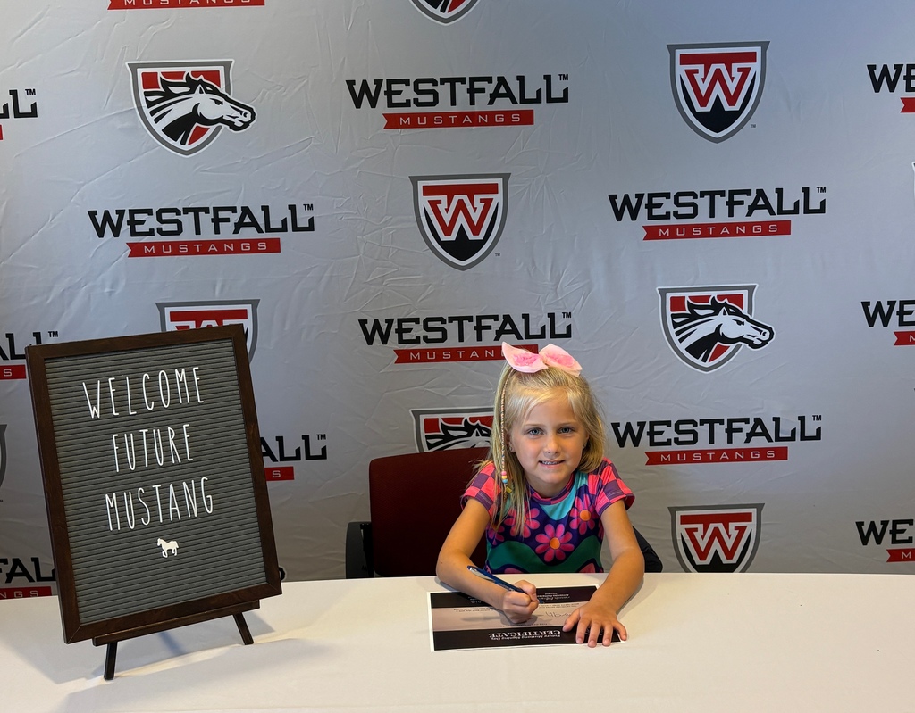 Kindergartener signing a certificate with the Westfall backdrop in the background and a sign that reads Welcome Future Mustang