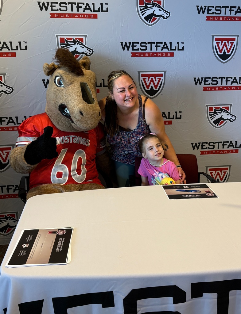 Kindergartener and mom signing a certificate with the Westfall backdrop in the background and a sign that reads Welcome Future Mustang