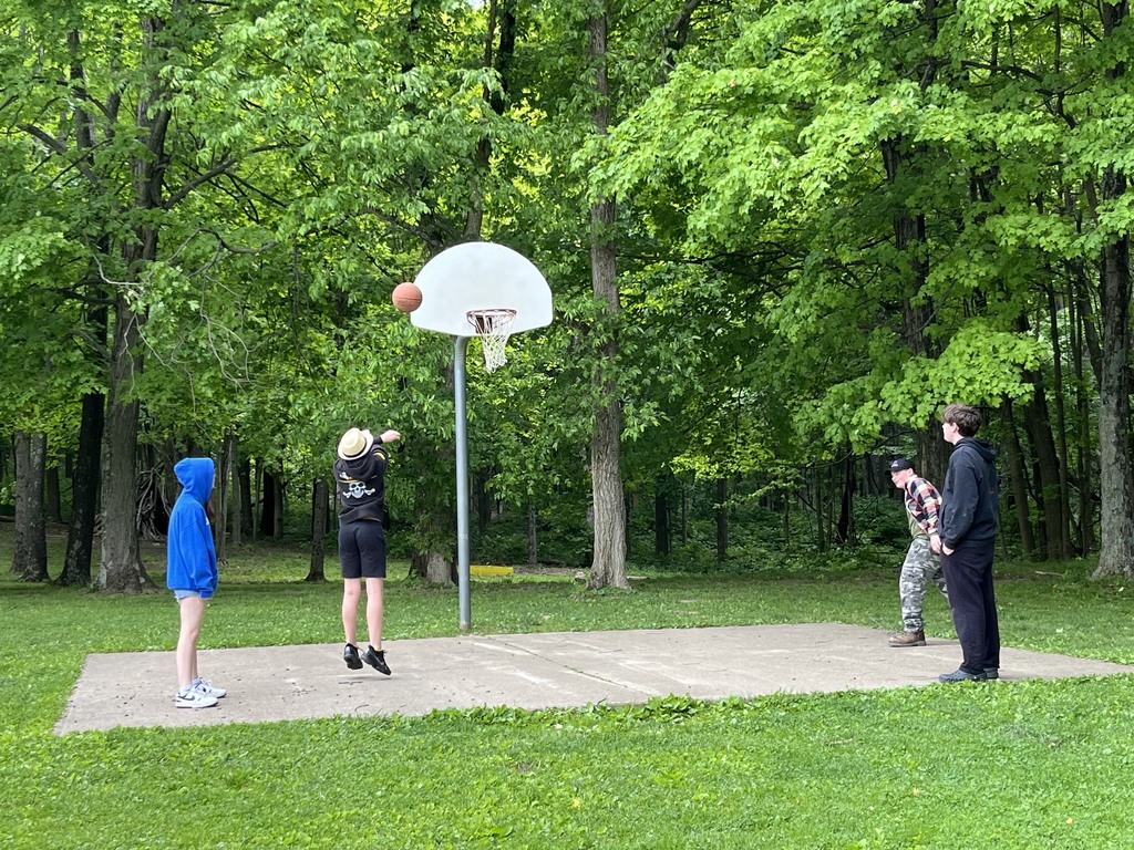 Students playing basketball in a wooded area