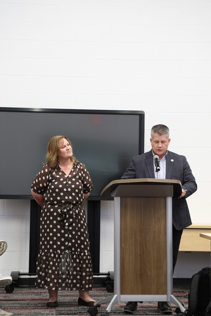 Ms. Bethany Treece standing beside Mr. Fife who speaks at a podium in the Community Room