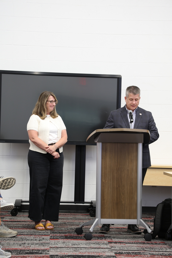 Ms. Karen Wing standing beside Mr. Fife who speaks at a podium in the Community Room