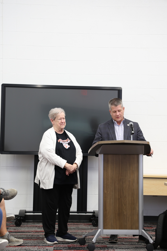 Ms. Carole Moore standing beside Mr. Fife who speaks at a podium in the Community Room