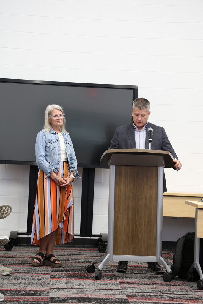 Ms. Marci Wippel standing beside Mr. Fife who speaks at a podium in the Community Room