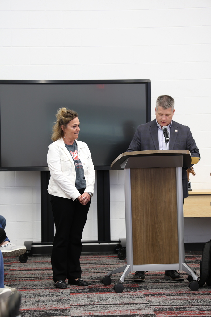 Ms. Judy Blum standing beside Mr. Fife who speaks at a podium in the Community Room