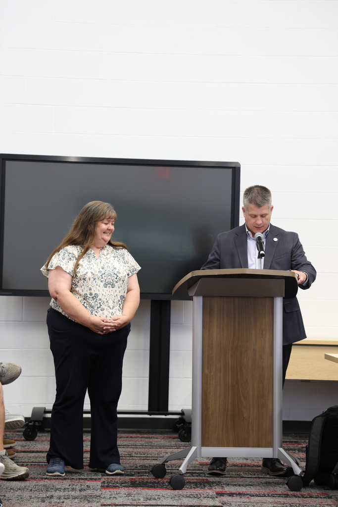 Ms. Marcia Ruff standing beside Mr. Fife who speaks at a podium in the Community Room