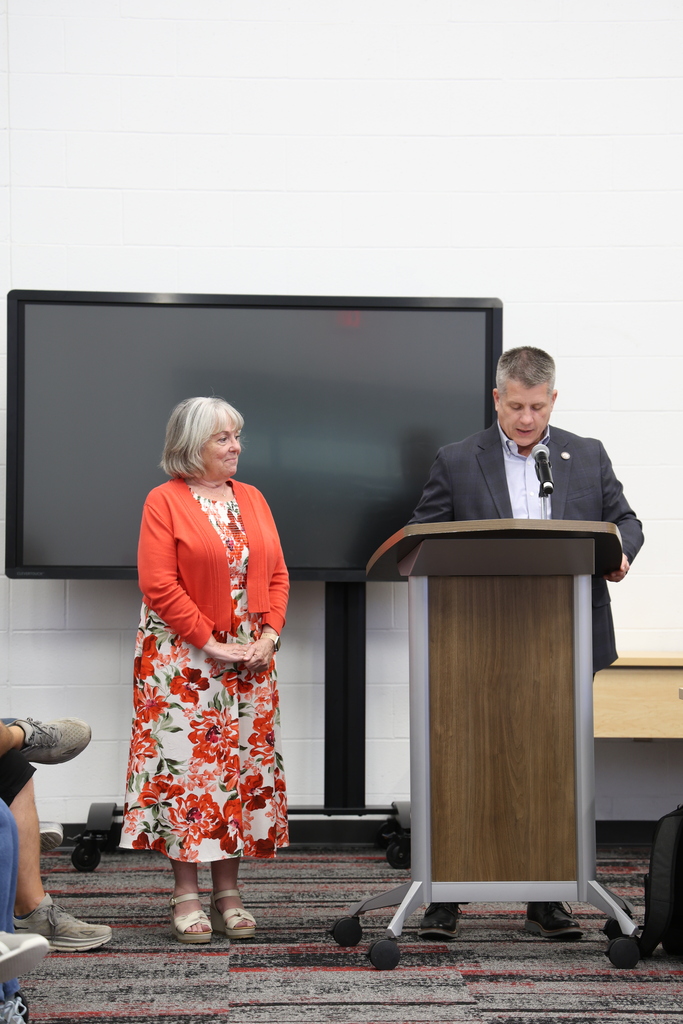 Ms. Tammy Cline standing beside Mr. Fife who speaks at a podium in the Community Room
