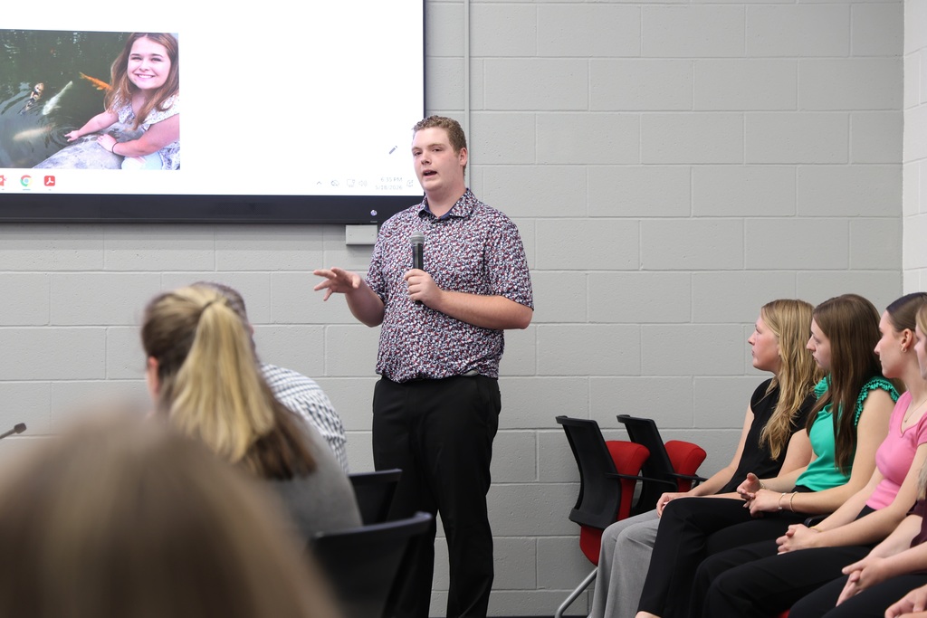 NHS Officer speaking into a microphone as they present their project that is shown on a large TV screen