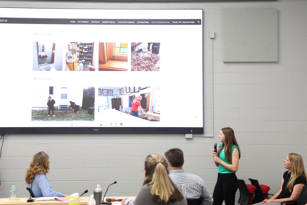 NHS Officer speaking into a microphone as they present their project that is shown on a large TV screen