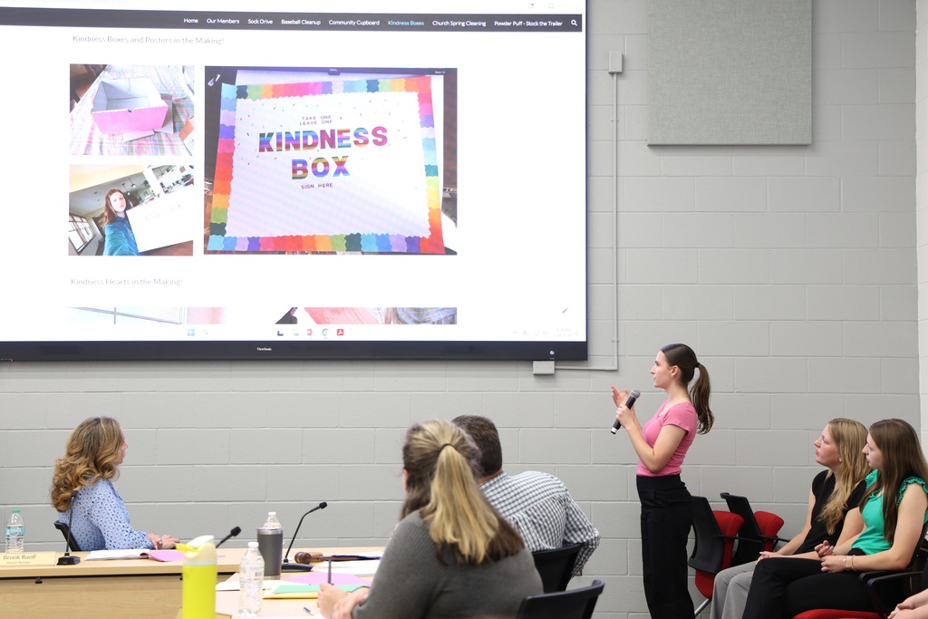NHS Officer speaking into a microphone as they present their project that is shown on a large TV screen