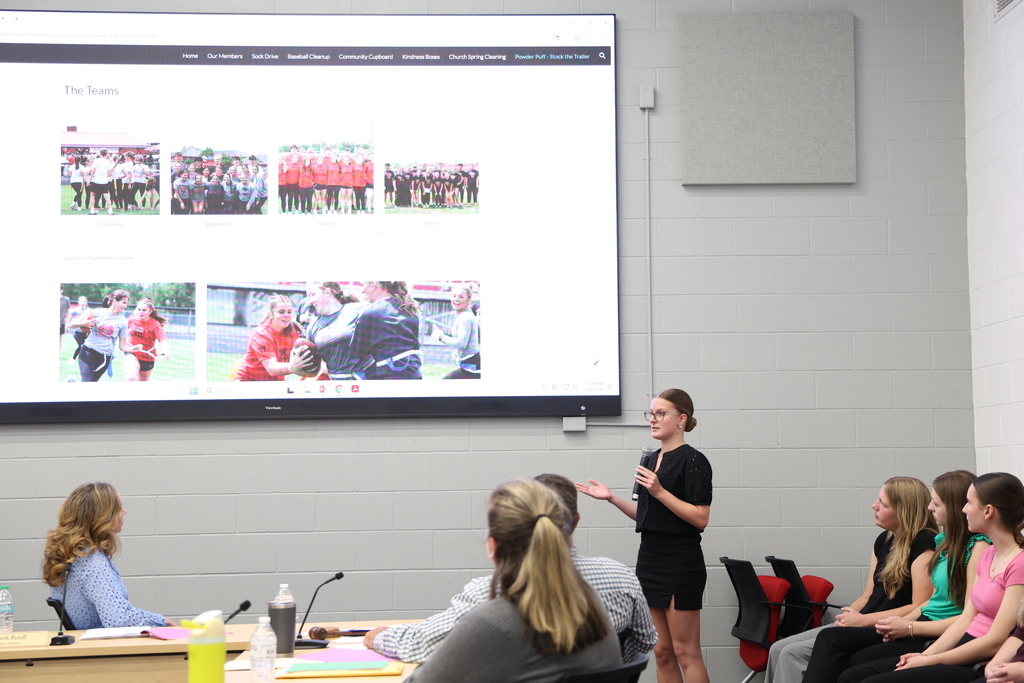 NHS Officer speaking into a microphone as they present their project that is shown on a large TV screen