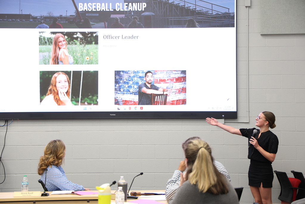 NHS Officer speaking into a microphone as they present their project that is shown on a large TV screen