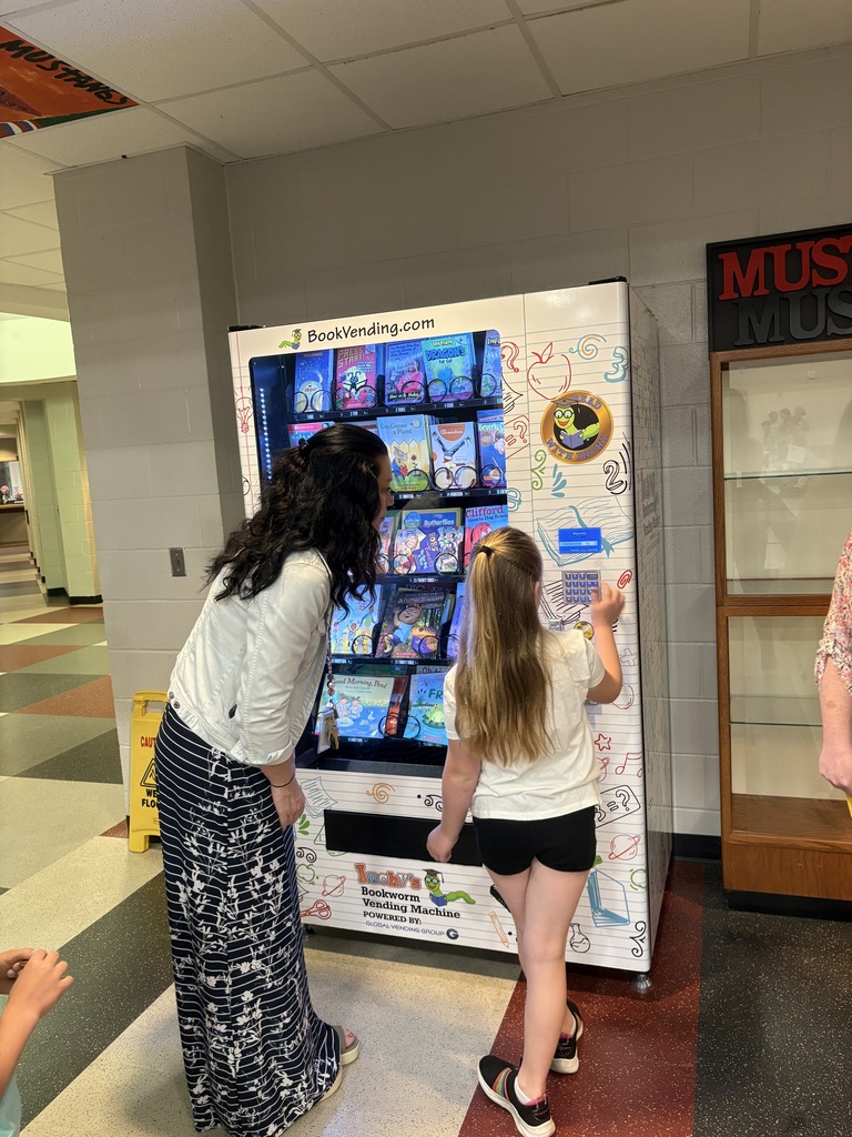Student selecting a book from the book vending machine while her teacher watches