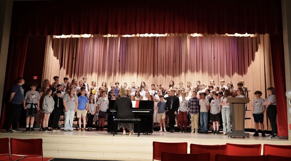Group photo of 5th graders with a music teacher sitting at the piano