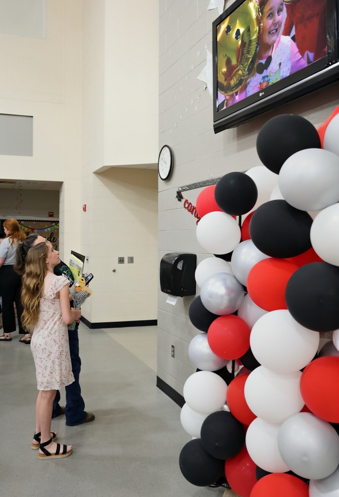 A mother and daughter watch a video on a tv screen that hangs high on a wall