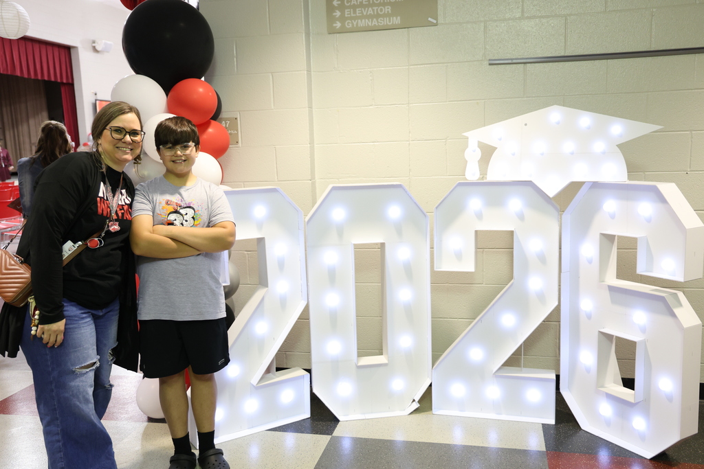 A mother and son pose in front of a lighted sign that reads 2026