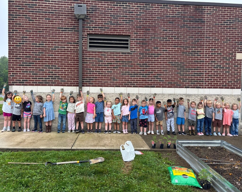 Students lined up against a brick wall waving