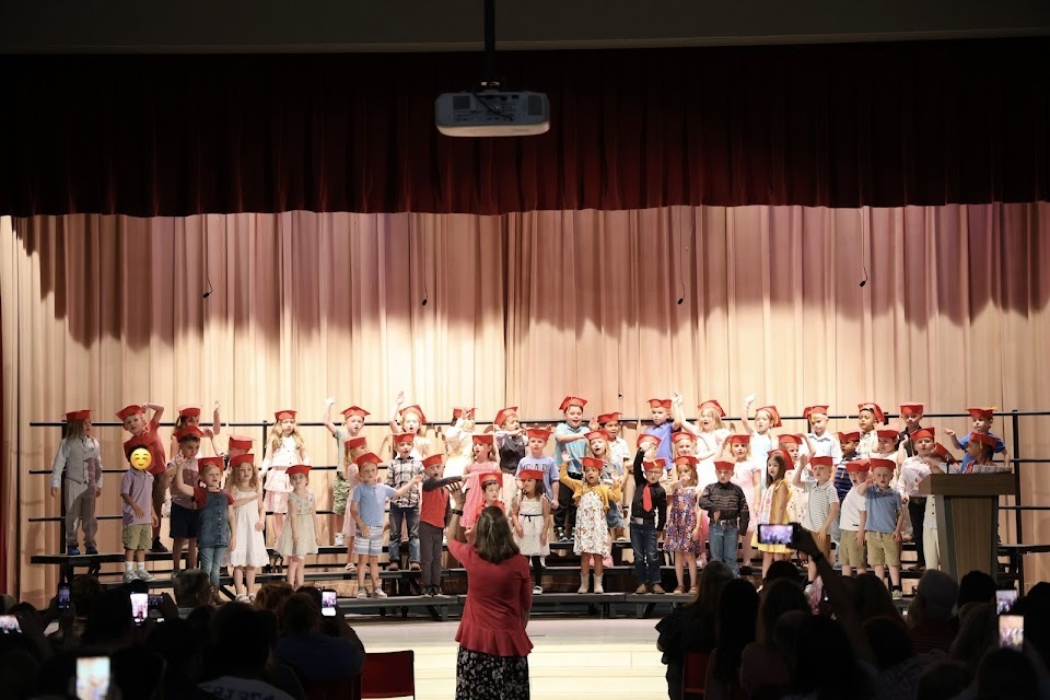 preschool class with gradation caps on singing a song on stage risers