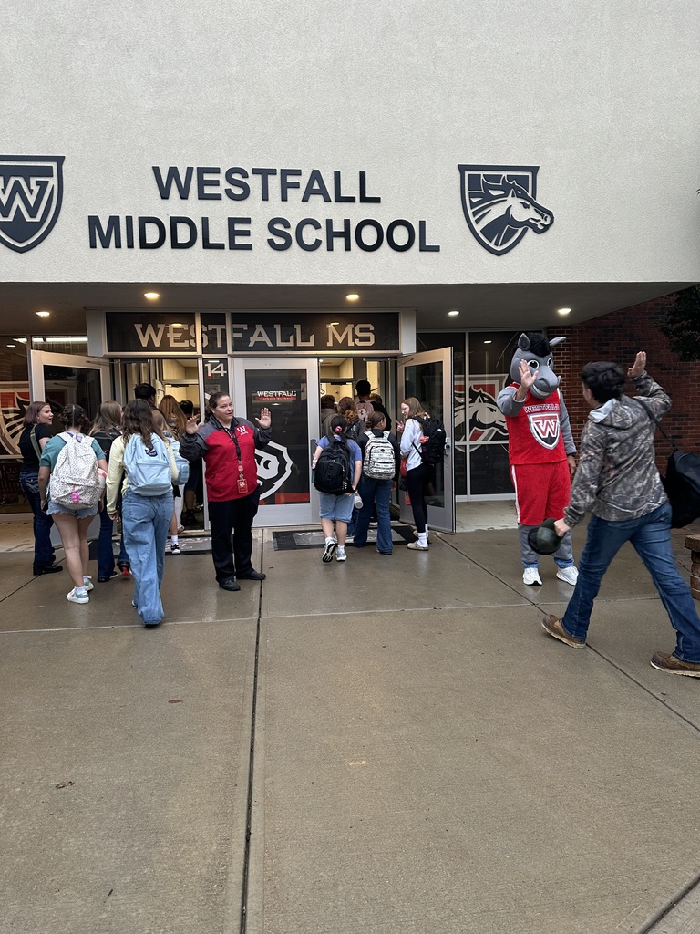 Students coming into the front of school building being greeted by Marty the Mustang